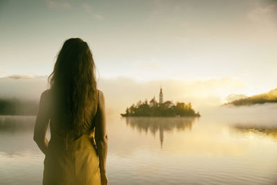 Woman in gray coat watching a sunrise among the fog on the shores of lake bled, slovenia vii