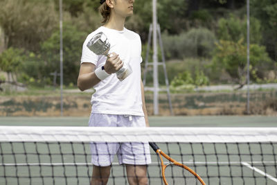 Unrecognizable young tennis player winner man holding a cup with strenght and a net in front of him