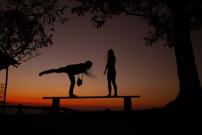 Silhouette women standing by tree against sky during sunset