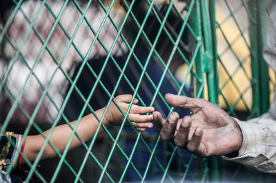 Close-up of girl hand reaching to father through fence
