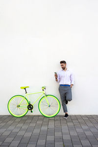 Young bearded man leaning against a white wall using the mobile phone