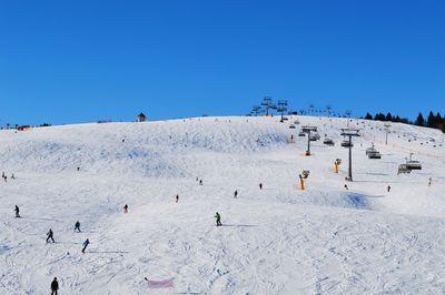 People skiing on snow against clear blue sky