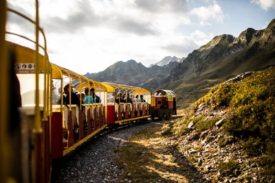 Small tourist train with people moving on railroad through mountains in summer day in pyrenees