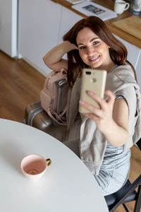 Portrait of smiling young woman using phone while sitting on table