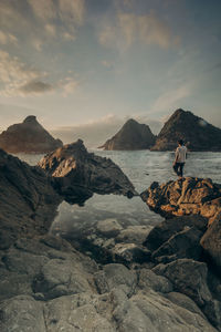 Man sitting on rock by mountains against sky