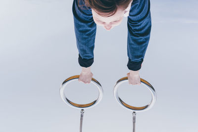 Upside down image of child holding gymnastic rings against gray background