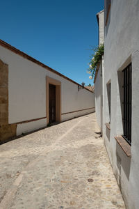 Footpath amidst buildings against clear blue sky