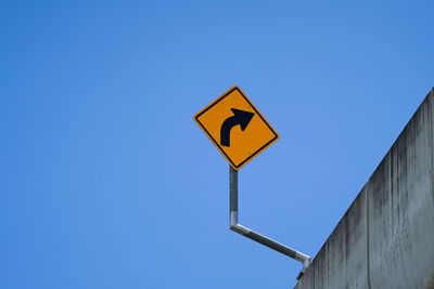 Low angle view of road sign against clear blue sky