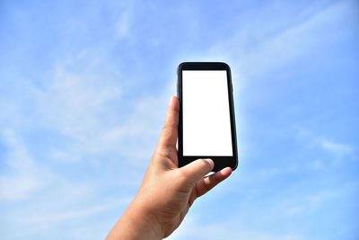 Cropped hand holding mobile phone against blue sky