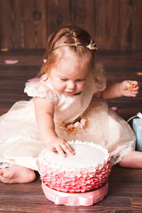 Cute baby girl with cake sitting on floor