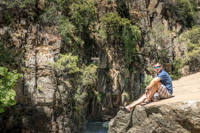 Side view of man sitting on rock by plants