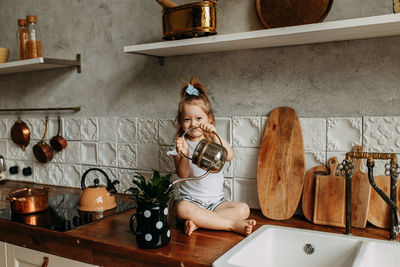 A little girl child takes care of watering a flower in a pot sitting on a kitchen cabinet at home