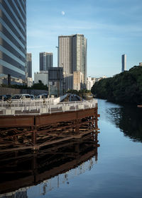 Modern buildings by river against sky in city