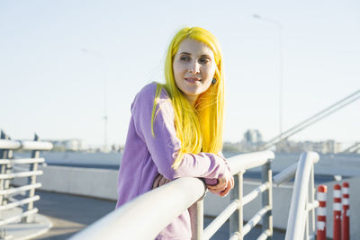 Portrait of smiling young woman against railing against sky