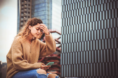 Woman using mobile phone while sitting by building