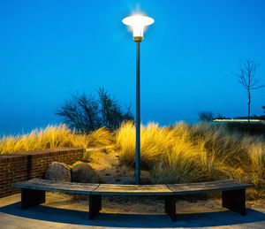 Illuminated street light against clear blue sky