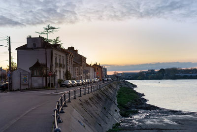 Buildings by sea against sky during sunset