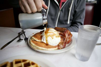 Midsection of man pouring syrup on pancake while sitting on table