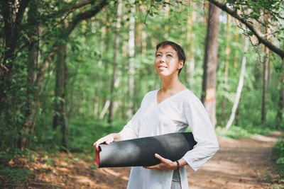 Smiling young woman standing by trees in forest