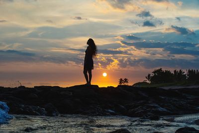 Man standing on rock by sea against sky during sunset