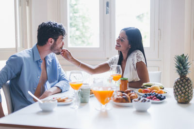 Smiling woman feeding breakfast to boyfriend at home