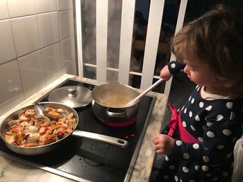 High angle view of girl cooking food on induction cooktop in kitchen