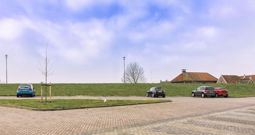 Cars on road by field against sky