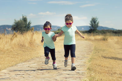 Siblings standing on field against sky