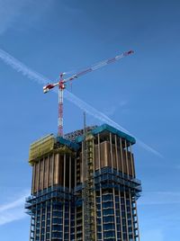 Low angle view of crane by building against blue sky