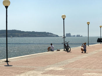 People sitting on bridge over river in city against clear sky