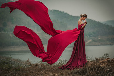 Side view of woman wearing red gown by lake