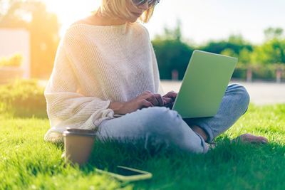  adult woman texting laptop, sitting on the grass outside in park. working and drinking coffee. 