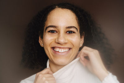 Portrait of smiling woman wearing turtleneck against brown background