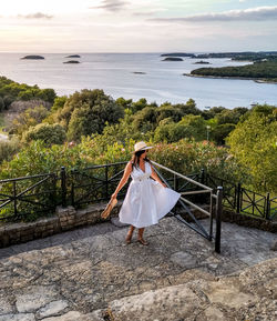 Woman standing on railing by sea against sky