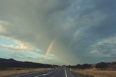 Rainbow over road against sky