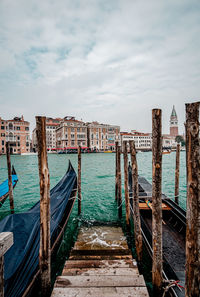 Wooden posts in canal against cloudy sky