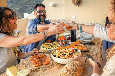 Cheerful friends toasting drinks while having food at table