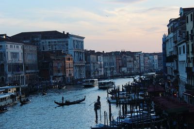 Boats in canal amidst buildings against sky during sunset