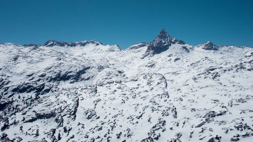 Low angle view of snowcapped mountains against clear blue sky