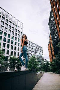 Low angle view of woman jumping against buildings in city
