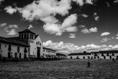 People walking on field by buildings against sky