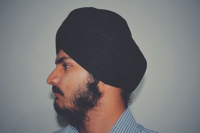 Profile view of young man wearing turban by white wall