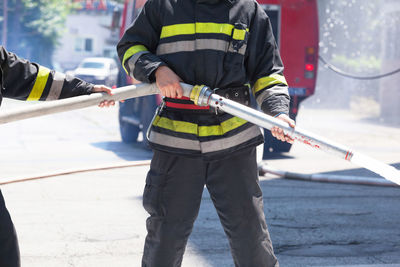 Midsection of firefighters holding fire hose