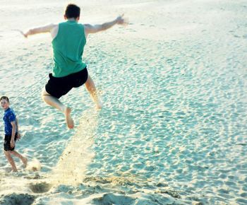 Rear view full length of man jumping at sandy beach