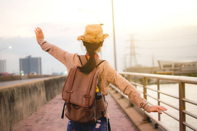 Rear view of woman with arms outstretched standing on bridge against sky