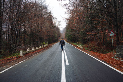 Rear view of man on road amidst trees during autumn