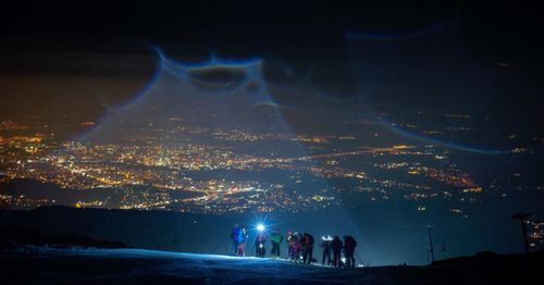 People at illuminated city against sky at night