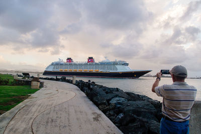 Rear view of man photographing cruise ship sailing in river