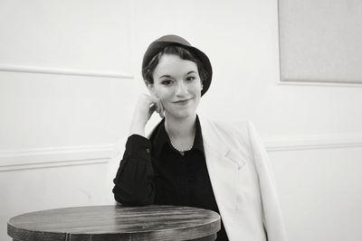 Portrait of smiling young woman sitting against wall