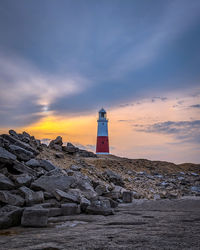 Lighthouse on building by sea against sky during sunset